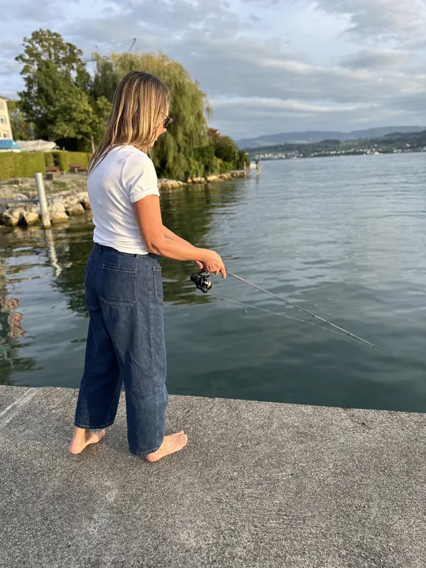 Teilnehmerin wirft barfuss vom Ufer aus die Rute in den See