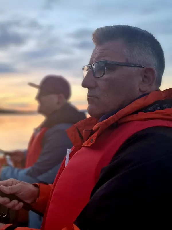 Zwei Reiseteilnehmer mit Schwimmwesten fischen im Abendlicht vom Boot aus