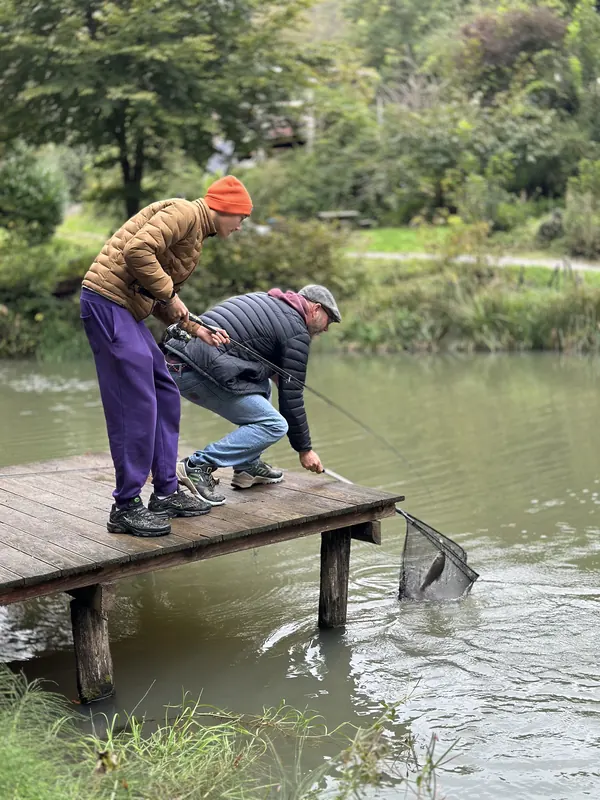 Teilnehmer landen vom Holzsteg aus einen Fisch mit dem Kescher
