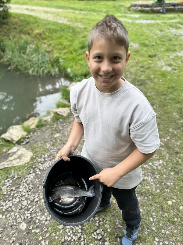Strahlender Junge zeigt seine Forelle im Eimer