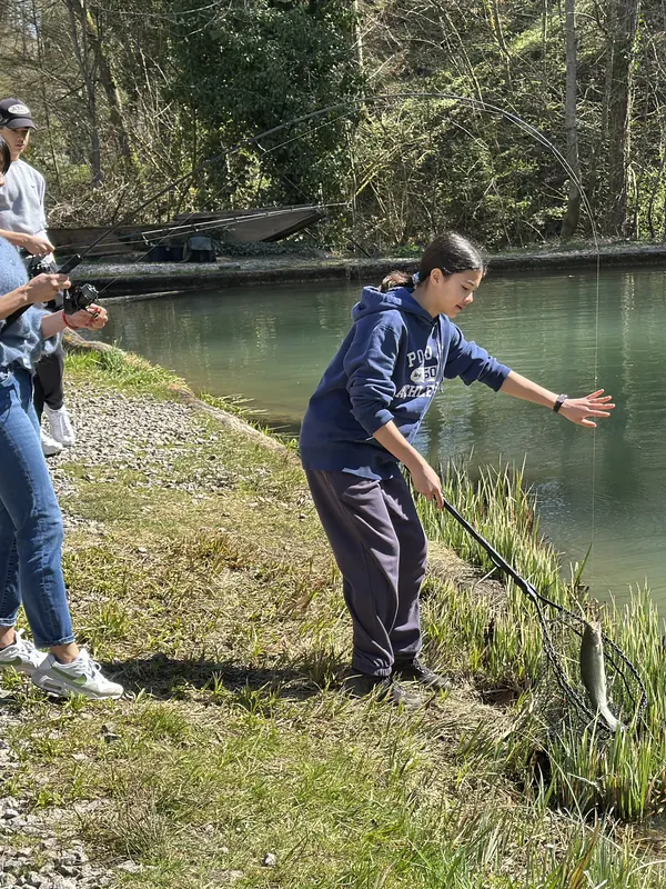 Jugendliche landet am Teich ihre erste Forelle mit dem Kescher