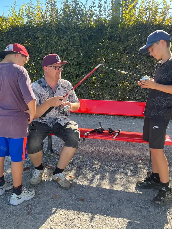 Instruktor zeigt zwei Jungen auf der Bank am See, wie die Rute funktioniert