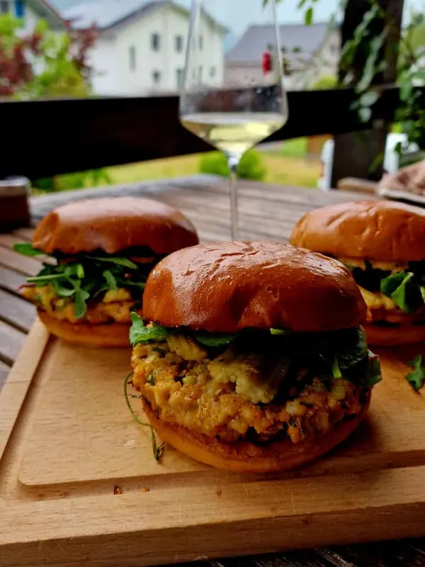 Selbstgemachte Fischburger auf dem Holzbrett mit einem Glas Weisswein