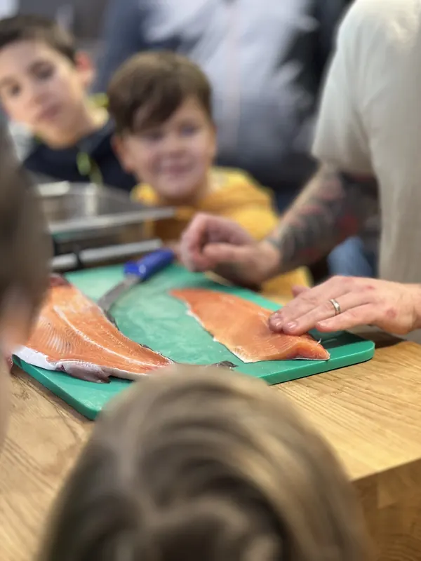 Frisch geschnittene Forellenfilets auf dem Brett, Kinder schauen dem Instruktor gespannt zu