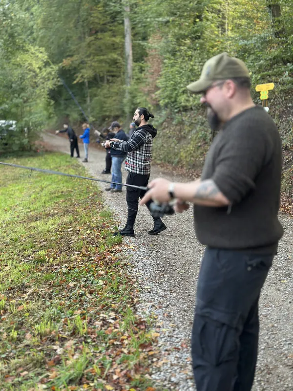 Teilnehmende fischen konzentriert am Waldweg entlang des Teichs