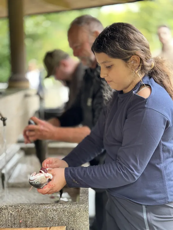 Mädchen hält stolz ihre frisch gefangene Forelle am Brunnen